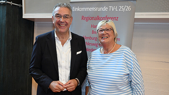 Ein Mann und eine Frau stehen vor einem grauen Aufsteller und blicken in die Kamera