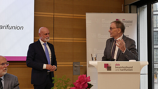 Zwei Männer in Anzügen unterhalten sich auf einer Bühne.