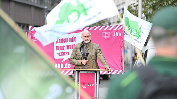 Volker Geyer Ein Mann steht im Mittelpunkt des Bildes und spricht in ein Mikrofon