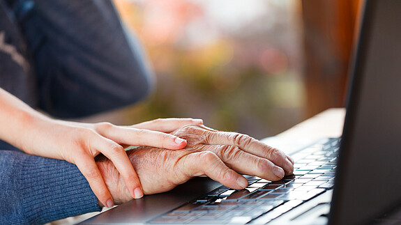 Internationaler Tag der älteren Menschen am 1. Oktober: Senioren sind nicht „von gestern“ Die Hand einer älteren Person liegt auf dem Mauspad eines Laptops. Auf der Hand liegt die eine jüngeren Person.