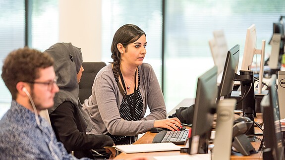 Büro Blick in ein Büro auf einen jungen Mann und zwei Frauen, eine von ihnen trägt ein Kopftuch. Alle schauen auf ihre Computer-Bildschirme