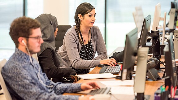 Büro Blick in ein Büro auf einen jungen Mann und zwei Frauen, eine von ihnen trägt ein Kopftuch. Alle schauen auf ihre Computer-Bildschirme