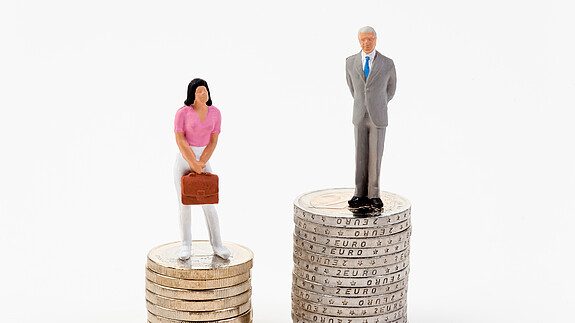 Kreutz: „Der Arbeitsmarkt muss attraktiver sein als der Heiratsmarkt“ Das Foto zeigt eine männliche und eine weibliche Figur, die auf Münzstapeln stehen. Der Stapel der männlichen Figur ist deutlich höher.