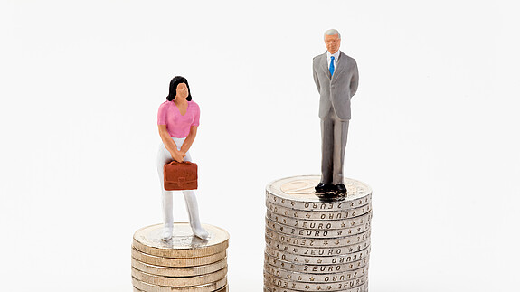Kreutz: „Der Arbeitsmarkt muss attraktiver sein als der Heiratsmarkt“ Das Foto zeigt eine männliche und eine weibliche Figur, die auf Münzstapeln stehen. Der Stapel der männlichen Figur ist deutlich höher.