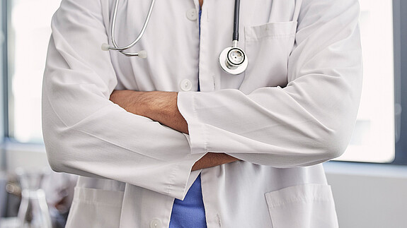 Gesundheitswesen ist Daseinsvorsorge und kein Sparposten Das Foto zeigt einen Arzt, er hat die Arme verschränkt.