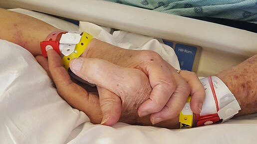 Das Foto zeigt zwei Hände - eine einer gesunden Person, eine einer kranken Person. 