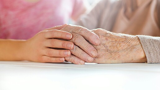 Foto einer jungen Hand, die eine ältere Hand umschließt.