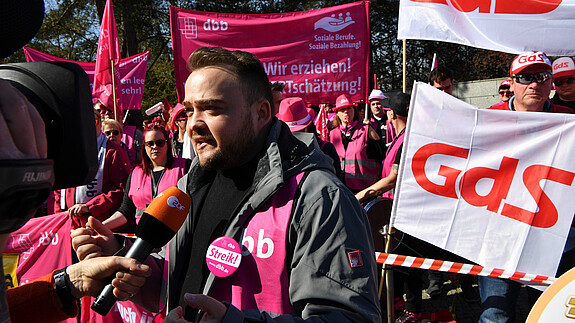 Matthäus Fandrejewski dbb jugend dbb jugend Chef Matthäus Fandrejewski steht vor Demonstrierenden in Potsdam und gibt dem Fernsehsender ZDF ein Interview zu den Tarifverhandlungen für den öffentlichen Dienst von Bund und Kommunen.