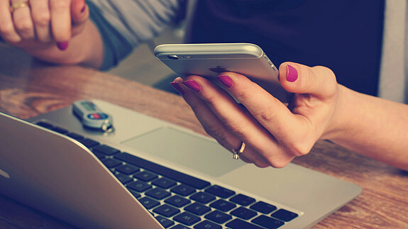 Faire KI und transparente Algorithmen für Beschäftigte Eine Person sitzt vor einem Laptop und hat ein Handy in der Hand