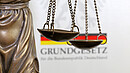 Nahaufnahme einer Justitia vor dem deutschen Grundgesetzbuch