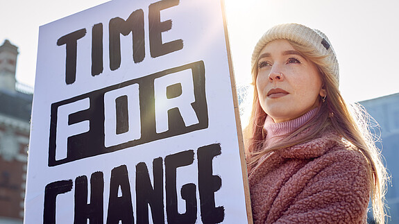 Weltfrauentag dbb jugend Eine junge Frau hält bei einer Demonstration ein Plakat mit der Aufschrift "Time for Change" hoch.