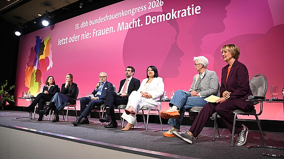 Menschen sitzen auf Stühlen auf einer Bühne und diskutieren miteinander.