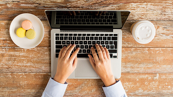 Deutsche Rentenversicherung: Nächste Sozialwahl auch online möglich Das Foto zeigt eine Laptoptastatur, man sieht noch den Bildschirm und Finger, die auf der Tastatur tippen.